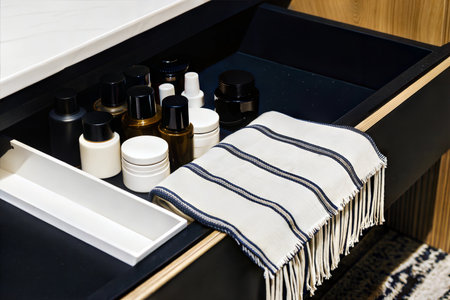Open drawer with various cosmetics and skincare products, neatly arranged. A striped towel with tassels adds a touch of elegance.の写真素材