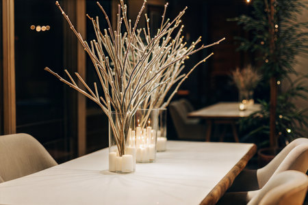 Elegant centerpiece with lit candles and branches with fairy lights in glass vases on a table.の写真素材