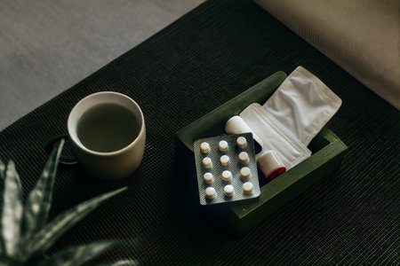 A cup of tea, blister pack of pills, and balm on a dark green textured table.  Relaxing atmosphere.の写真素材