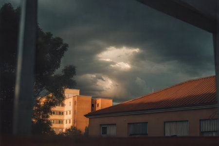 A view through a window of apartment buildings under a dramatic sunset sky with dark clouds.の写真素材