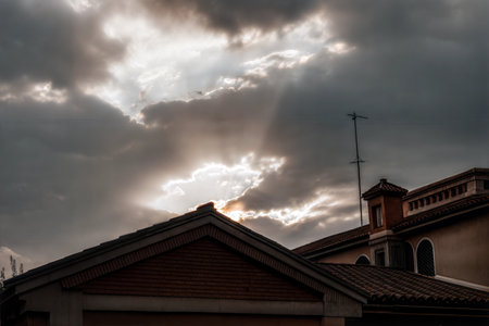 Sunbeams breaking through dark clouds over a building's rooftop.の写真素材