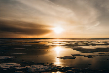 Melting ice on a lake at sunset, with warm colors in the sky and water reflecting the light.の写真素材