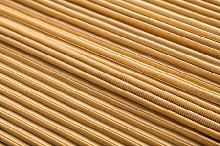 Close-up view of parallel golden rods with a textured surface, arranged in diagonal lines creating an abstract pattern.の写真素材