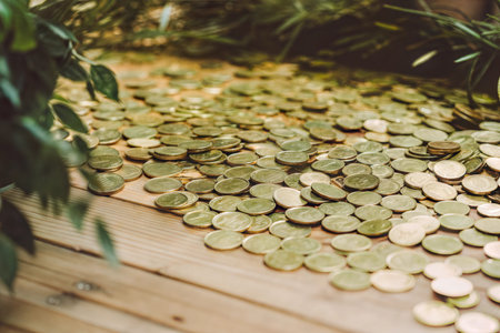 Many coins are scattered on a wooden surface, partially obscured by green plants.