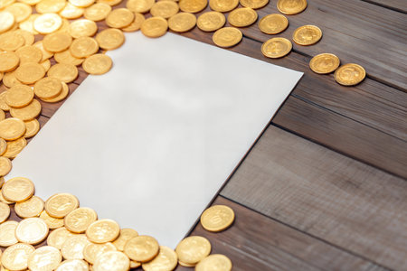 White paper on wooden surface surrounded by gold coins.  Plenty of copy space.の写真素材