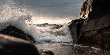 Stunning view of ocean waves breaking against dark rocks during a vibrant sunset. Water splashes and sunlit foam are visible.の写真素材
