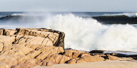 Dramatic waves breaking against the rugged coastline. White water and spray fill the foreground,...