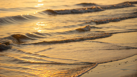 Soft waves gently lapping the shore at sunset, creating a warm, golden glow.の写真素材