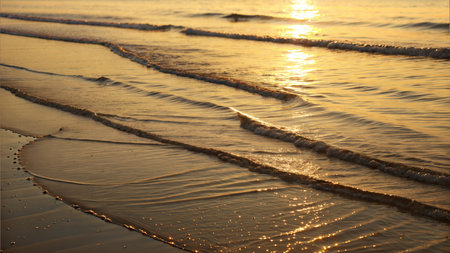 Soft waves gently rolling onto the beach at sunrise, sunlight reflecting on the water's surface.の写真素材