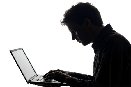 Side view silhouette of a man sitting and working on his laptop at night.の写真素材