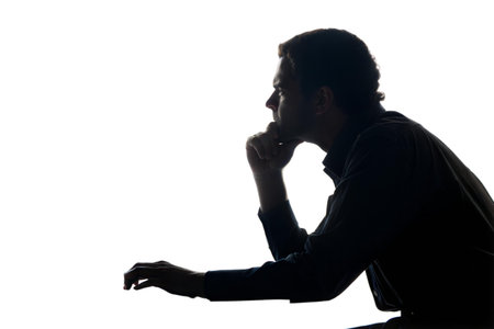 A man sits in profile, his face lit from the side, appearing thoughtful and contemplative. The image...