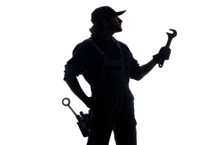 Silhouette of a mechanic holding a wrench against a black background. He is wearing a uniform and cap.の写真素材