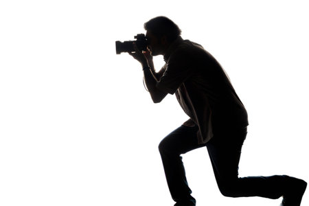Silhouette of a photographer kneeling and taking a picture against a completely black background.