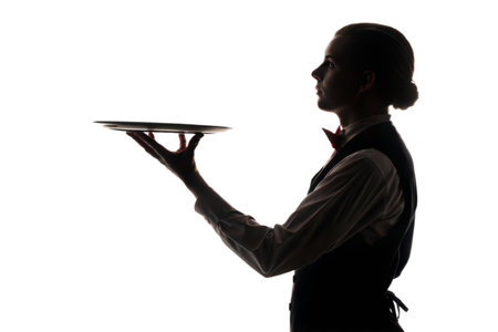 A dramatic silhouette of a waiter in profile, holding a tray, set against a black background.の写真素材