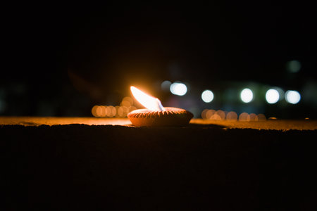 A single candle burns brightly in the darkness, casting a warm glow. Bokeh lights are visible in the background.の写真素材