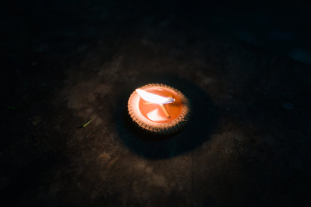 A single candle burns brightly in the darkness, casting a warm glow on the surrounding surface.の写真素材