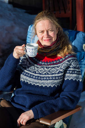 Close up of young pretty Norwegian woman enjoying some winter sunshine and a cup of coffee in a traditional Norwegian jumperの写真素材