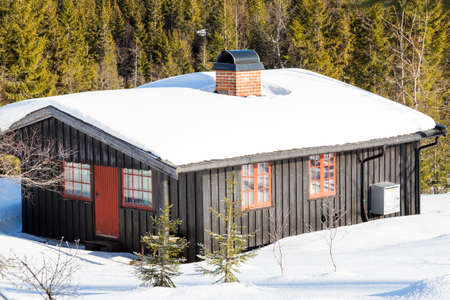 Typical black Norwegian cabin covered in snow in the forest North of Oslo - side viewのeditorial素材