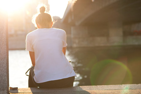 The girl sits in the rays of the setting sun in an urban environment