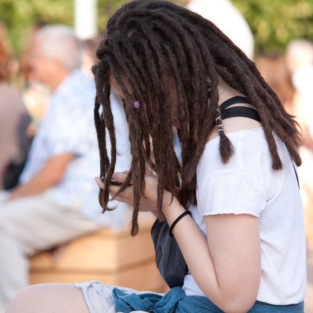 A girl with a fashionable youth haircut from dread sitting and communicate on her mobile phone