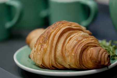 appetizing croissant on a plate and on a background of green cups, will help you to quickly have a...