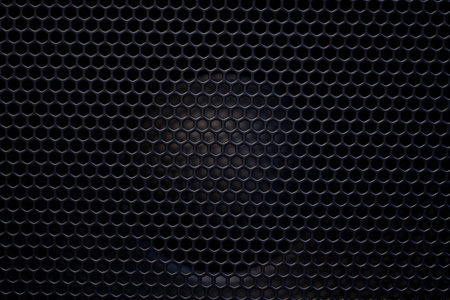 The speaker of a musical column hidden behind a grid with a pattern of rhythmically arranged holes
