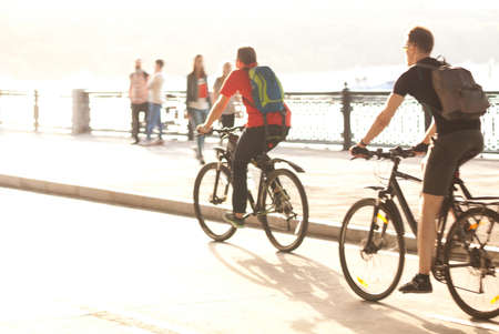 two men ride bicycles on the summer sunny city embankmentの写真素材