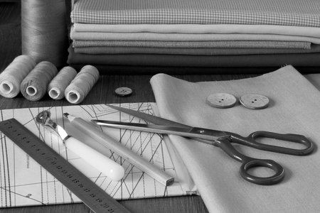 tailor's scissors, a stack of fabric cuts, a pencil, sewing threads and a folded paper pattern lie...