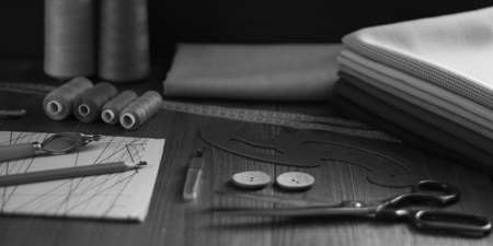 tailor's scissors, a stack of fabric cuts, a pencil, sewing threads and a paper pattern lie on a wooden table awaiting creative ideasの写真素材