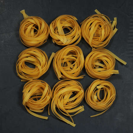 textured background created by dry raw curled noodles lying on a black tableの写真素材