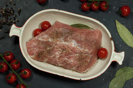 piece of meat lies in a cast iron bowl and is prepared for stew. a cast-iron bowl of steet meat on the table, cherry tomatoes, peppers and dry bay leaves are on the table.の写真素材
