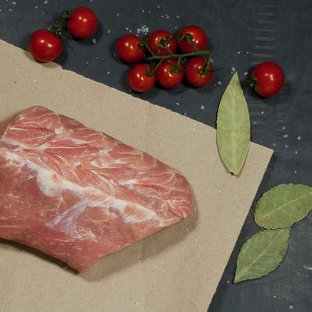 piece of meat on paper is on the table to cooking dinner. there is also a branch of cherry tomato and dry bay leaves.の写真素材