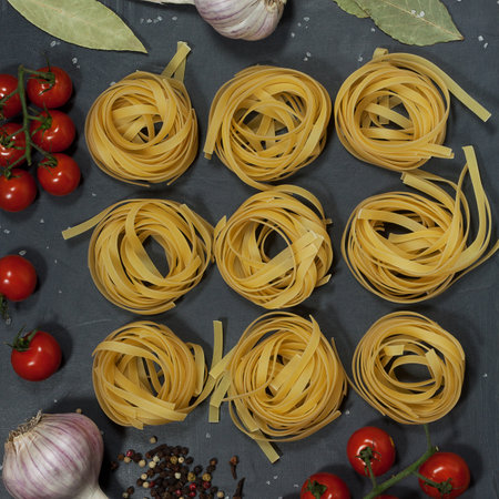 on a black table are raw dry rolled noodles, cherry tomato branches, garlic, bay leaves and peppers. everything is prepared for the cooking of a delicious lunch.の写真素材