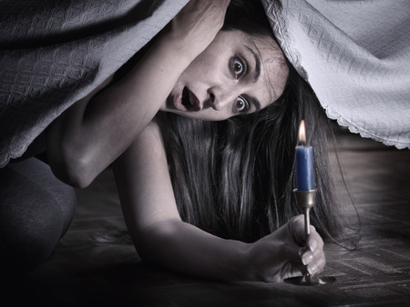 A young woman fear, looking under the bed and surprised at what she seesの写真素材