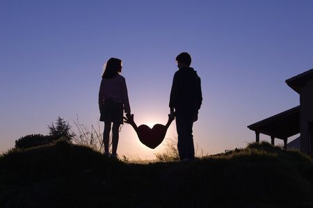 Silhouettes of two children holding a heart with their hands at duskの写真素材