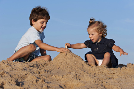 Two children have fun on the beach playing with the sandの写真素材