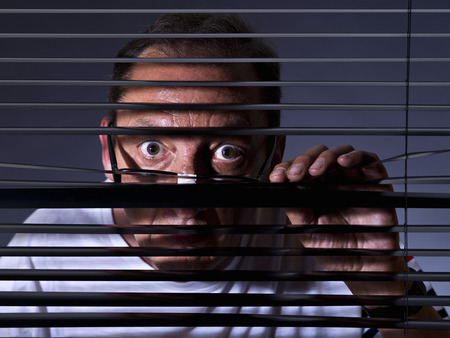 Vicious man looking sideways through venetian blindの写真素材