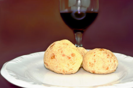 Brazilian typical food: Cheese Bread on a white plate and a glass of wine in the blurred backgroundの写真素材