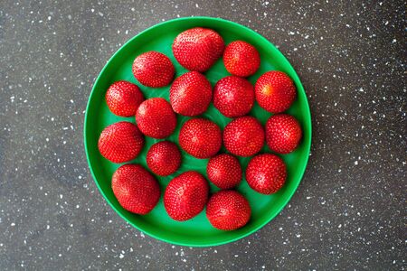summer strawberry on a black table lies on a green plate, top viewの写真素材