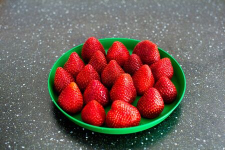 summer strawberries on a black table lies on a green plateの写真素材