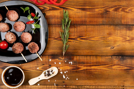 Meat balls on wooden skewers lie on a black plate. Sauce, spices, rosemary. Top.の写真素材