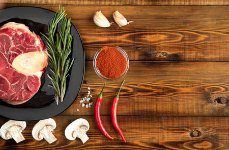 Raw meat on a black plate. Pepper, garlic, mushrooms, rosemary, sauce. Board. Top.の写真素材