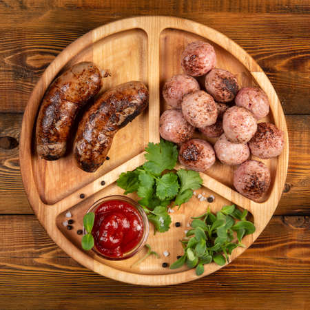 Fried sausages and meat balls with sauce and herbs on a wooden plate. Top.の写真素材