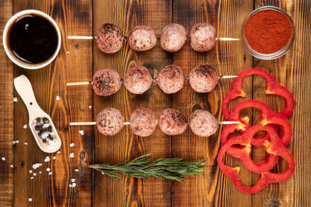 Meat balls on wooden skewers lie on the board. Sauce, spices, paprika, rosemary.の写真素材