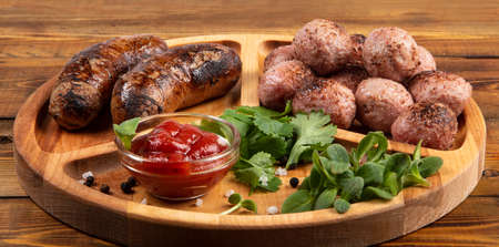Fried sausages and meat balls with sauce and herbs on a wooden plate.の写真素材