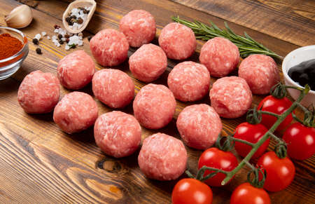 Raw meat balls, cherry tomatoes, garlic, pepper, sauce, rosemary, spices on the board.の写真素材