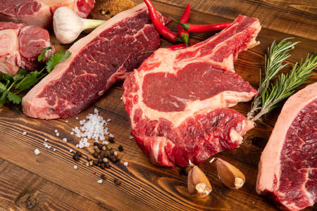 Pieces of raw meat on a wooden table. Chili pepper, garlic, rosemary, spices.の写真素材