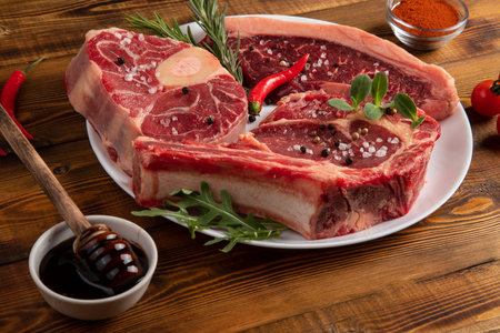 Chunks of raw meat on a white plate. Chili pepper, rosemary, onion, spices. Wooden table.の写真素材