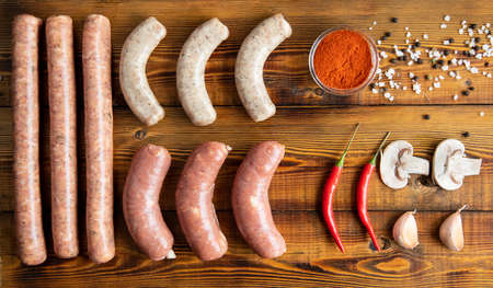Meat sausages on a wooden table. tomatoes, chili peppers, garlic, mushrooms, spices. Top view.の写真素材