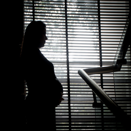 NEW DELHI, INDIA - MARCH 2017 : a silhouette of a mother expecting a baby in front of a large glass windowのeditorial素材